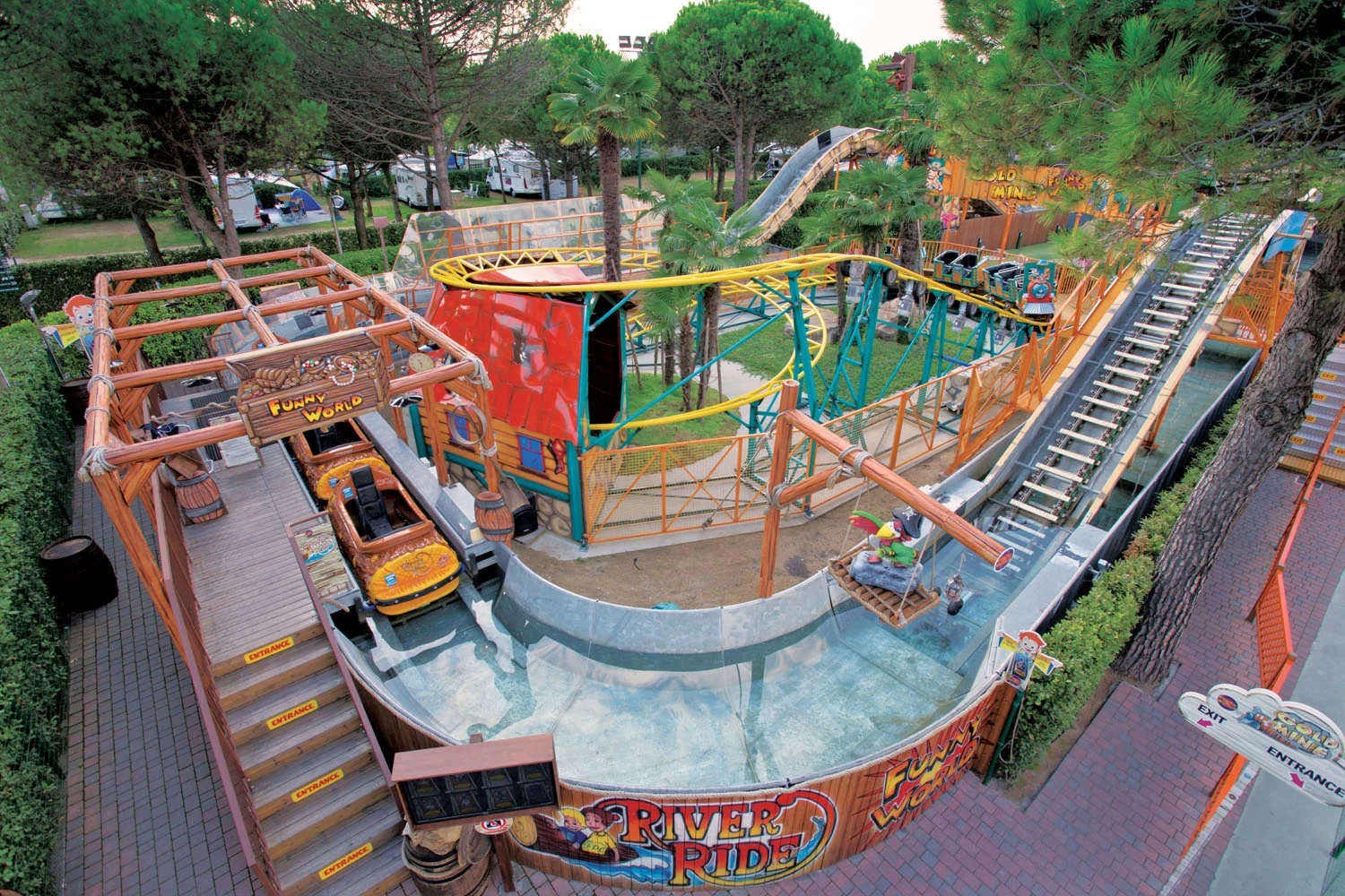 At Union Lido, a log boat journey rises along a slope next to the tracks and a vibrant roller coaster in a forested amusement zone with campers.