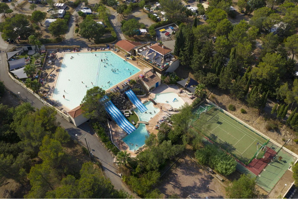 At Domaine de la Noguiere, there is a spacious swimming pool featuring slides, encircled by trees and camping sites within a recreational area.