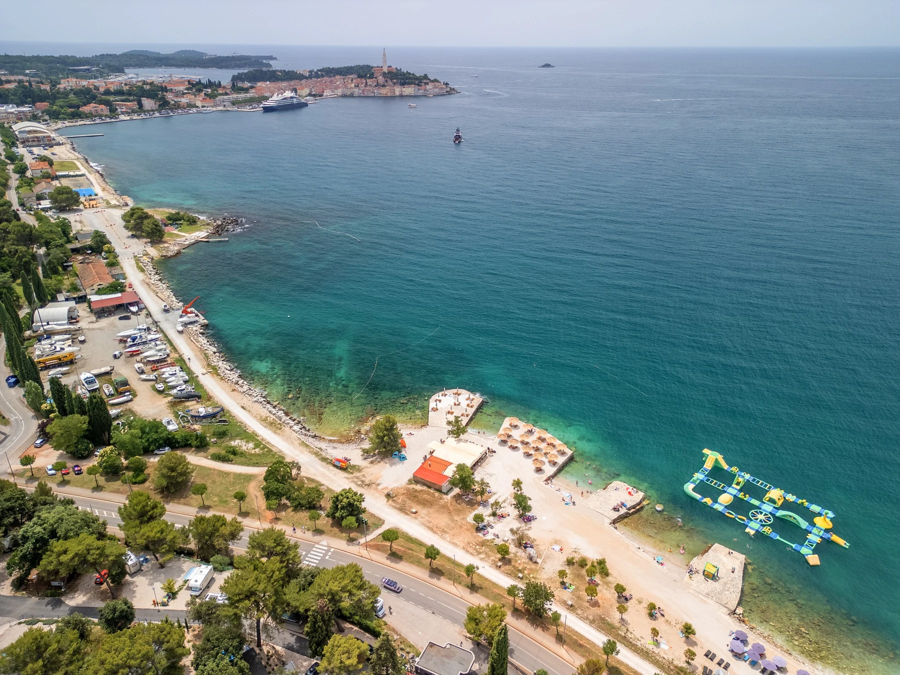 At Porton Nature Hideouts, an elevated perspective reveals a seaside region featuring shorelines, vessels, and a buoyant water amusement park adjacent to a town.