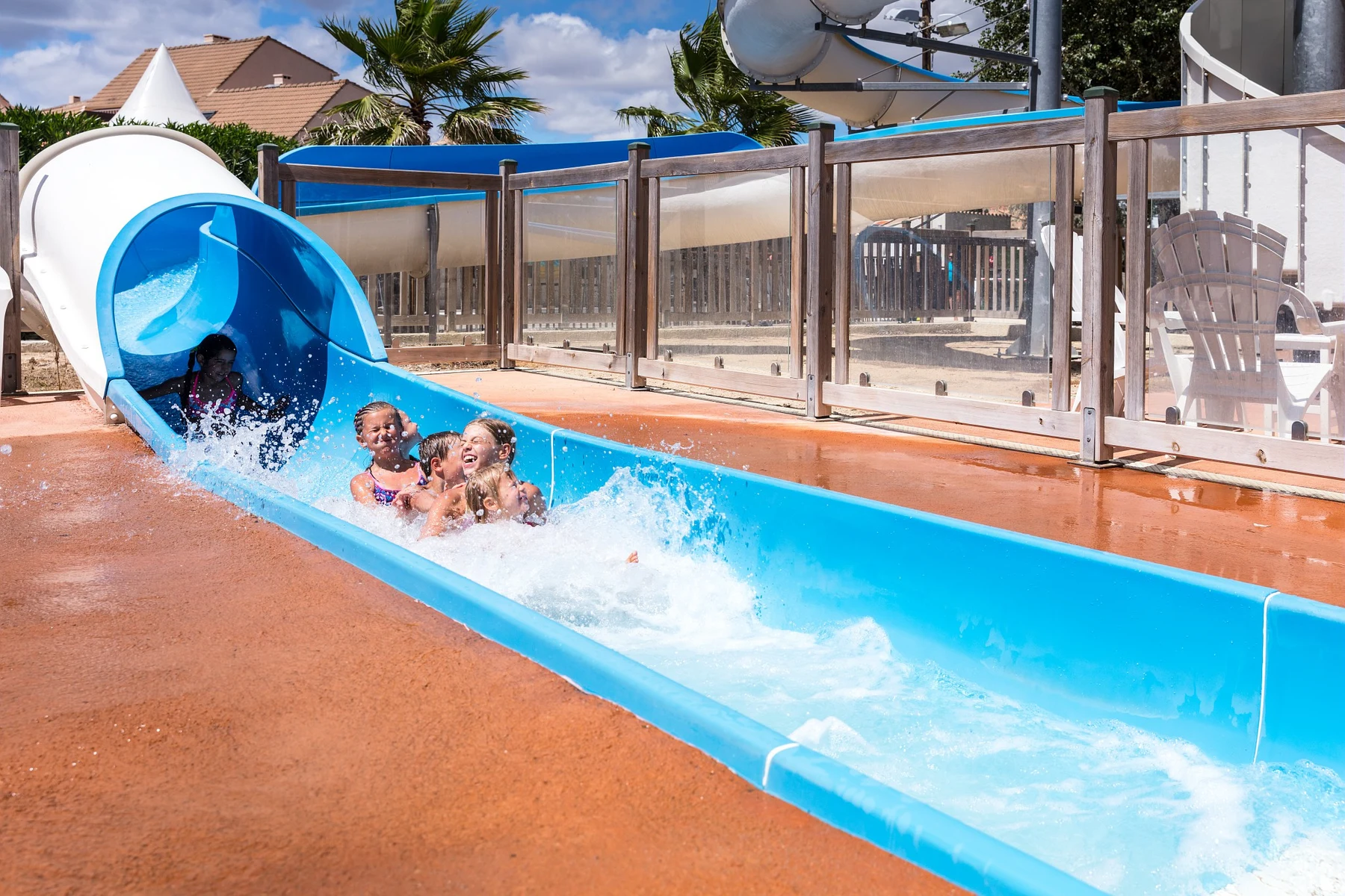 At Marvilla Parks Dunes et Soleil, kids glide down a blue water slide, splashing into a pool beneath a sunny sky.