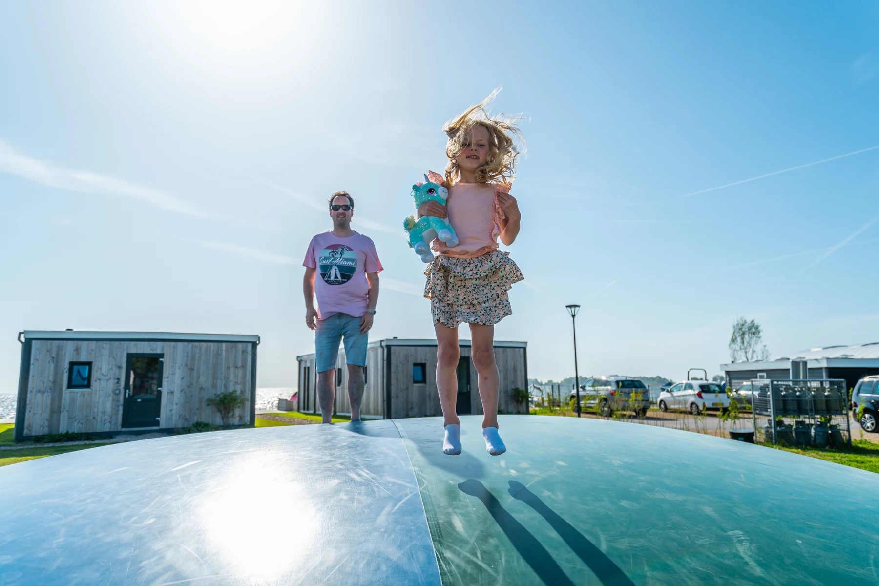 At Europarcs Enkhuizer Strand, a child leaps on an inflatable cushion while clutching a stuffed animal, watched by an adult under the sunny sky.