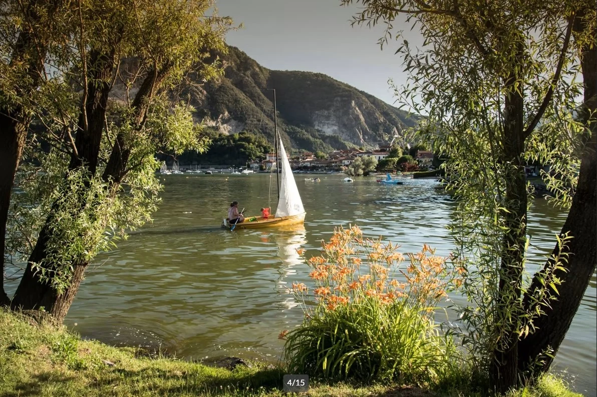 At Conca d’Oro Camping & Lodge, a petite sailboat glides over a serene lake, encircled by trees and far-off mountains.