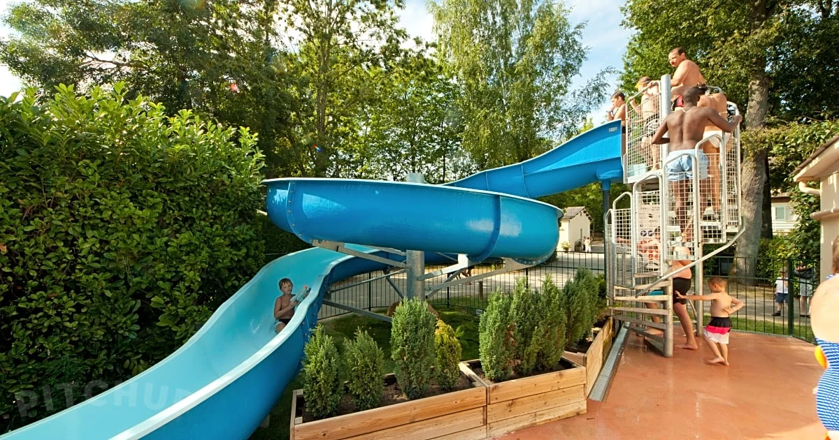 At Countrypark Touquin, children are gliding down a blue water slide while others are waiting on the steps in a green, tree-filled environment.