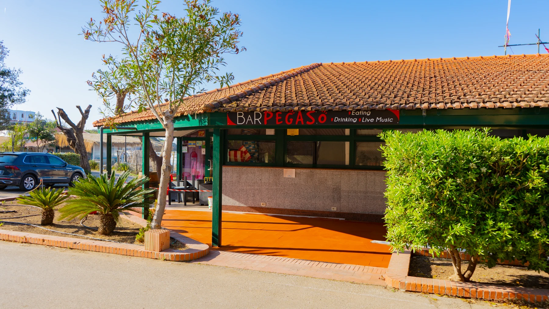 At Centro Turistico San Nicola, a tavern with a tiled rooftop is encircled by foliage and greenery, situated in a bright outdoor environment.