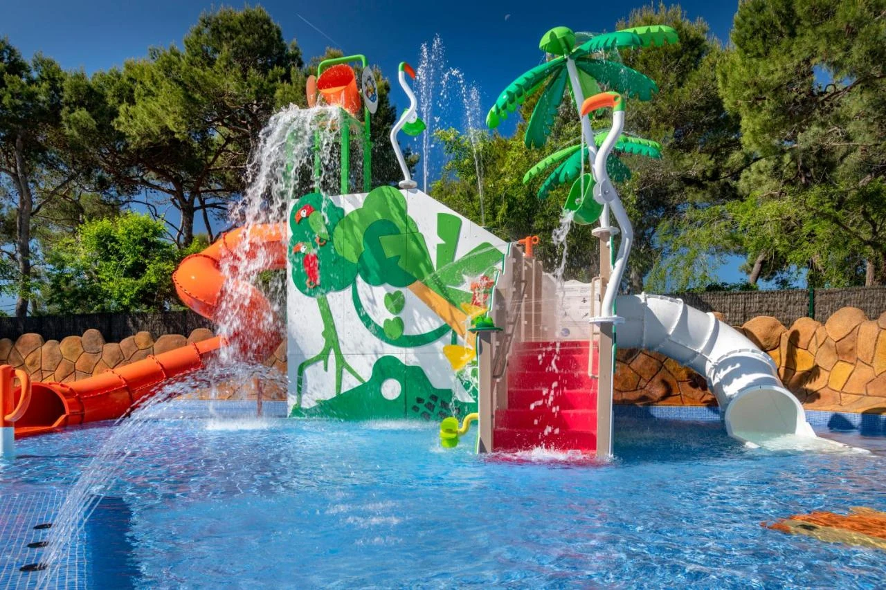 At Solmar, a vibrant water park design features slides and sprays, encircled by trees and lively murals.