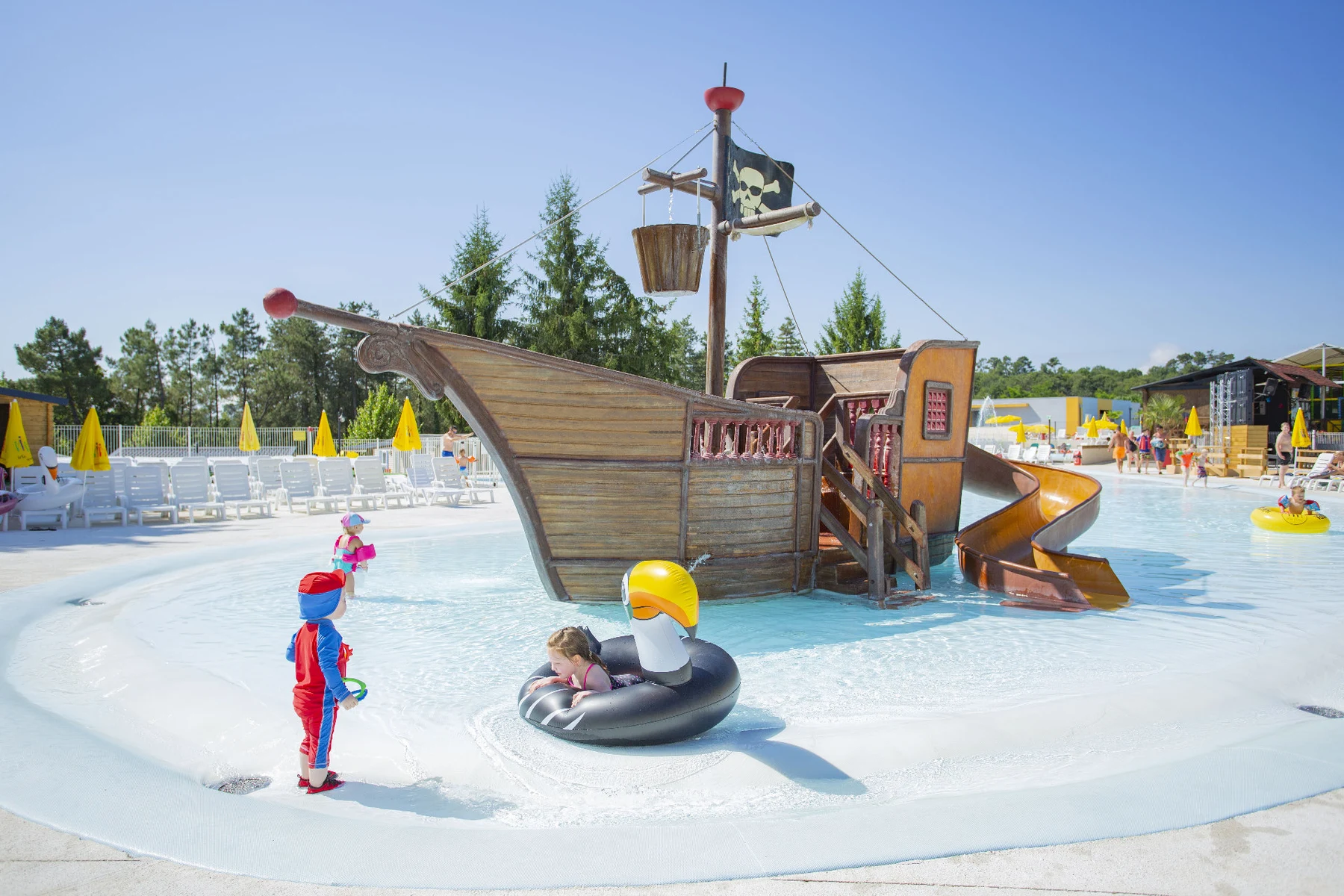 At Le Grand Dague, kids are enjoying themselves on a pirate ship-inspired water slide in a shallow pool encircled by lounge chairs and umbrellas.