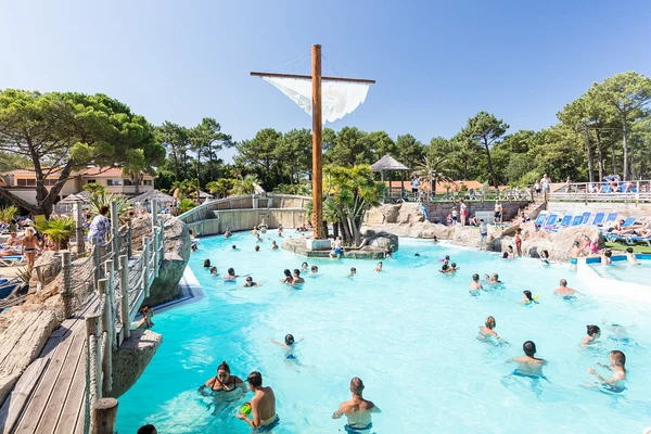 At Le Vieux Port, individuals are swimming in a pool encircled by deck chairs, trees, and a pirate ship structure.