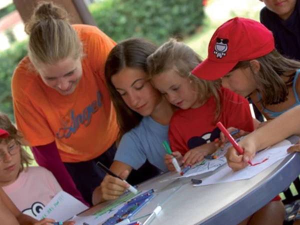 At River, children are coloring images at a circular table while an adult oversees them outside.