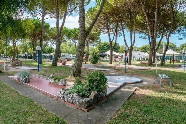 At Pra delle Torri, a mini-golf course is situated amidst trees, tents, and parked recreational vehicles.