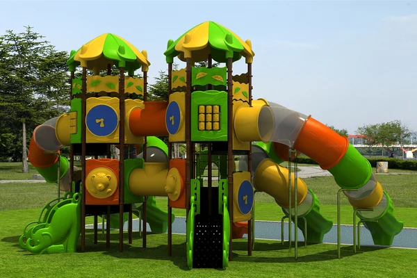 At the river campsite, there is a vibrant play structure featuring slides and tunnels, situated on a grassy area close to trees and a pathway.