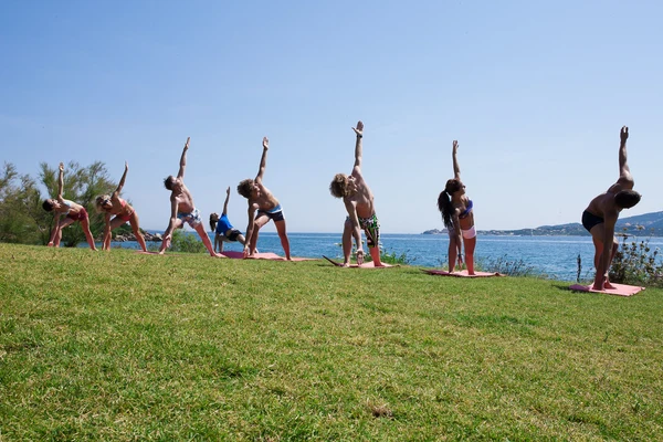At Isuledda, individuals are engaging in yoga on mats, extending their bodies outdoors on the grass with a backdrop of the ocean.