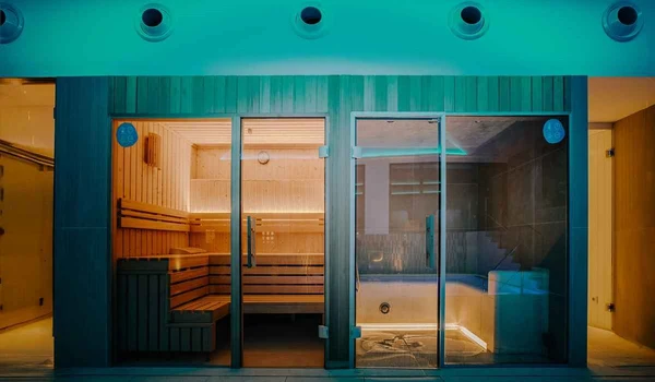 At Costa del Sol Glamping Village, a glass-enclosed sauna and a nearby hot tub are softly lit within a contemporary indoor wellness space.