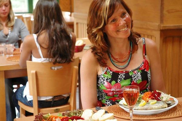 At Petite Suisse, a woman is grinning while enjoying a meal at a table with a dish of food and a drink, within a relaxed dining atmosphere.