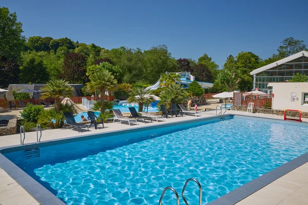 At Marvilla Parks Le Ty Nadan, there is a swimming pool accompanied by sun loungers next to a water slide, encircled by vibrant greenery and structures.