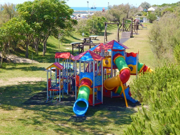 At Pra delle Torri, vibrant play structures featuring slides and climbing elements are nestled among trees and lush greenery.