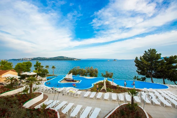 At Amadria Park Camping Trogir, a swimming pool features sun loungers and individuals unwinding, framed by the ocean and remote islands.