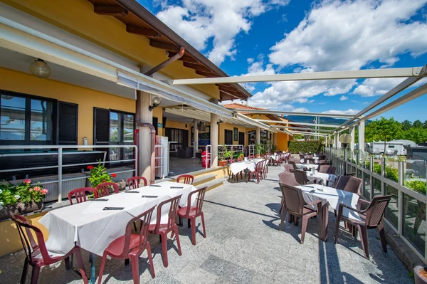 At Orchidea, outdoor dining tables adorned with white table linens are arranged along a patio beneath a partly cloudy sky, with caravans visible in the vicinity.