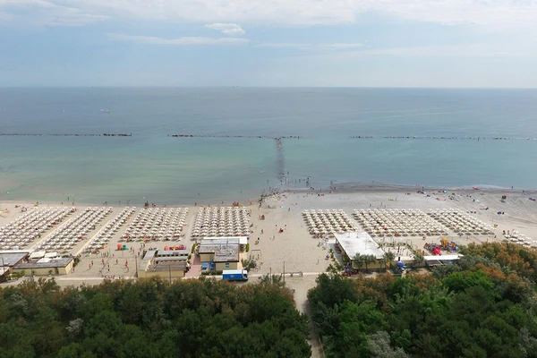 At Marina Family Village, rows of beach canopies stretch along the sandy coastline; individuals splash in the tranquil water set against a backdrop of blue skies.