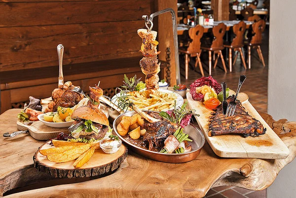 At Eurocamp Wilder Kaiser, an assortment of barbecued meats and accompaniments is displayed on rustic wooden tables within a warm, wooden dining environment.