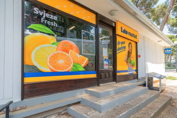 At Porton Nature Hideouts, the grocery store facade showcases colorful fruit visuals and promotional displays in a lush outdoor environment.