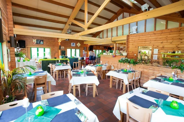 At Petite Suisse, dining tables adorned with white linens and green details are encircled by wooden walls and greenery.