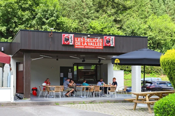 At Floreal la Roche, individuals are seated at outdoor café tables, dining and sipping beverages, encircled by lush vegetation and vehicles.