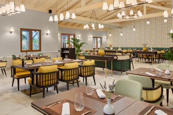 At Amadria Park Camping Sibenik, dining tables are set with contemporary chairs in a well-lit eatery adorned with floral wallpaper and decorative greenery.