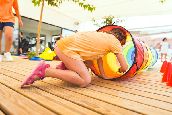 At Costa del Sol Glamping Village, a child is crawling through a vibrant tunnel on a wooden platform, encircled by cones.