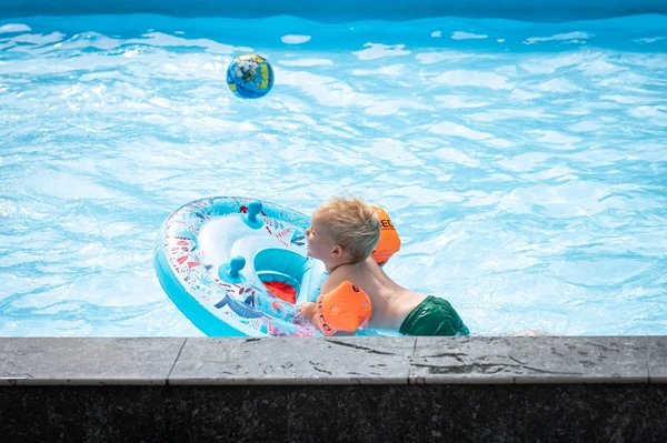 At Petite Suisse, a child is swimming with an inflatable ring and water wings in a pool, with a floating ball nearby.