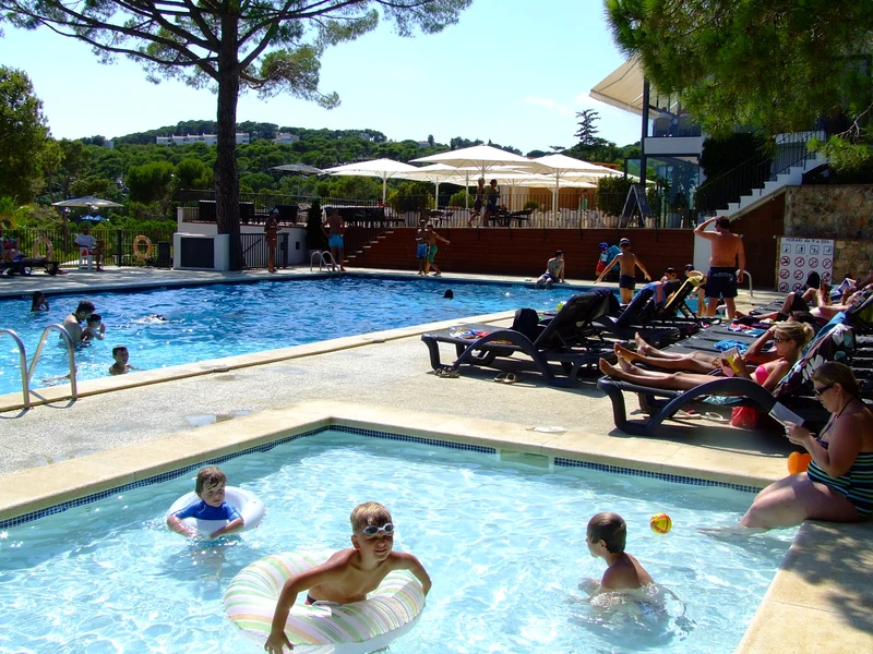 At Internacional de Calonge, youngsters are enjoying themselves in a swimming pool while grown-ups unwind on lounge chairs beneath umbrellas.