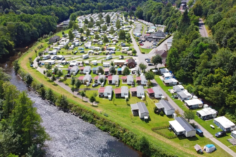 At Floreal la Roche, a riverside campsite featuring caravans and mobile homes is surrounded by vibrant green trees, forming a charming getaway.
