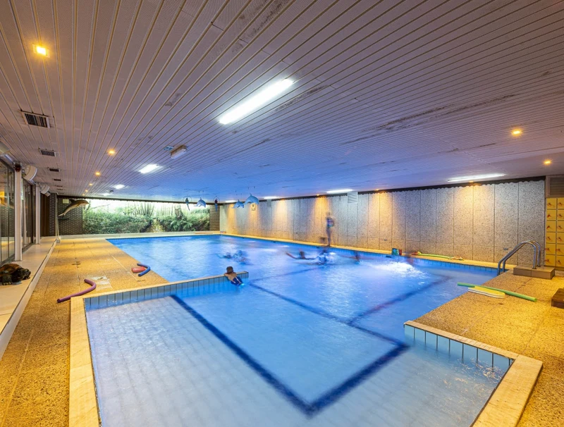 At Recreatieoord Wilhelm Tell, children are enjoying themselves in the water of the indoor swimming pool, with pool toys spread out around them.