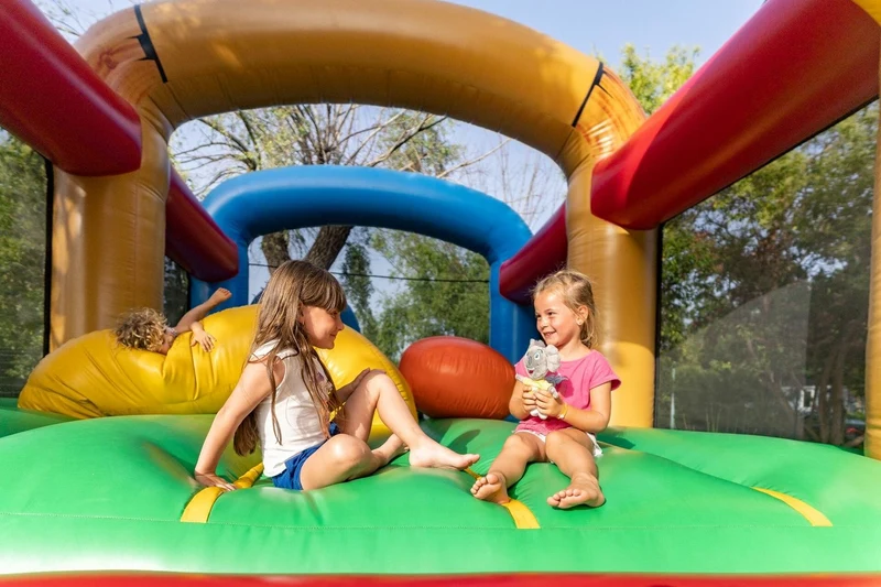 At Ondres Plage, two kids are playing in a vibrant inflatable castle, encircled by trees.
