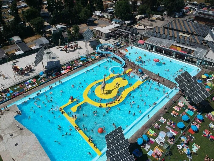 At Recreatieoord Wilhelm Tell, a swimming pool featuring waterslides is filled with individuals relishing a sunny day, encircled by sunbathing loungers and umbrellas.