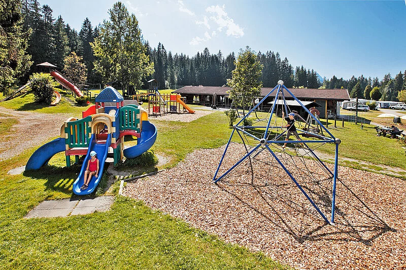 At Eurocamp Wilder Kaiser, kids are enjoying themselves on vibrant play structures in a lush park encircled by trees and cabins.