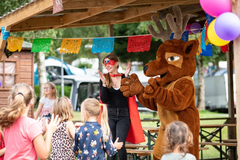 At Petite Suisse, an individual in a crimson mask and reindeer outfit claps, amusing children beneath a wooden shelter.